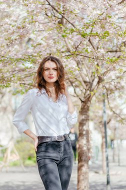 Beyaz gömlekli kız baharda çiçek açan sakura 'nın yanında duruyor.