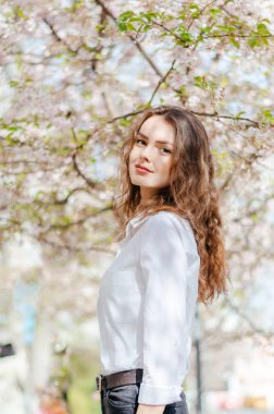 Baharda çiçek açan sakura çiçeğinin yanında beyaz gömlekli genç bir kızın fotoğrafı çekilir.