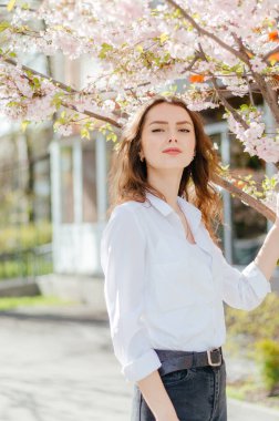 Beyaz tişörtlü kız sakura 'nın yanında duruyor. bahar, güneşli