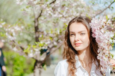 Güneşli bahar havasında beyaz gömlekli kız sakura 'nın yanında duruyor.