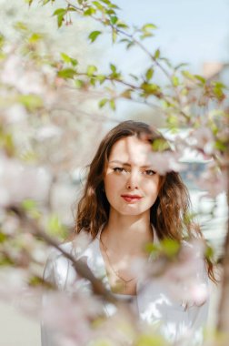 Güneşli bahar havasında beyaz gömlekli kız sakura 'nın yanında duruyor.