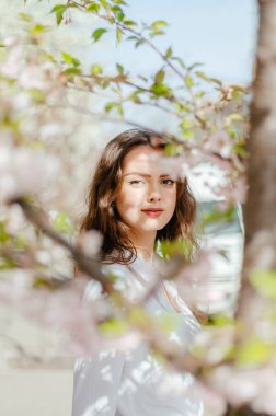 Güneşli bahar havasında beyaz gömlekli kız sakura 'nın yanında duruyor.
