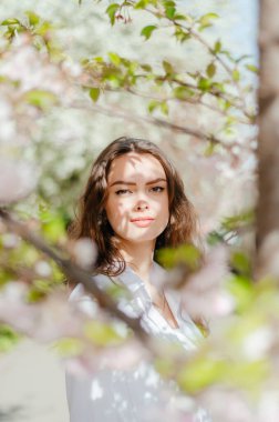 Güneşli bahar havasında beyaz gömlekli kız sakura 'nın yanında duruyor.