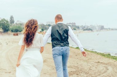 Erkek ve kadın düğün kıyafetleriyle sahilde koşuyorlar.