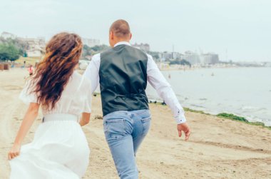 Erkek ve kadın düğün kıyafetleriyle sahilde koşuyorlar.