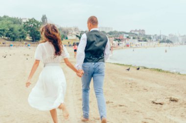 Erkek ve kadın düğün kıyafetleriyle sahilde koşuyorlar.