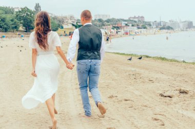 Erkek ve kadın düğün kıyafetleriyle sahilde koşuyorlar.