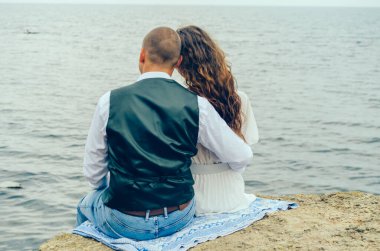 Erkek ve kadın bir taşın üzerinde oturup denize bakıyorlar.