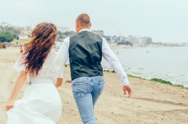 Erkek ve kadın düğün kıyafetleriyle sahilde koşuyorlar.