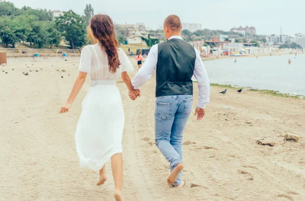 Erkek ve kadın düğün kıyafetleriyle sahilde koşuyorlar.