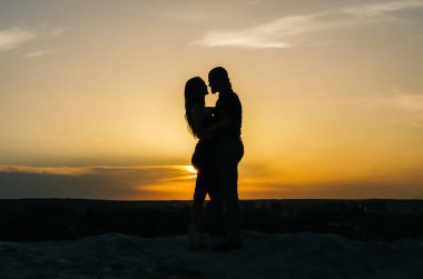 Gün batımında kucaklaşan sevgi dolu bir çiftin silueti.
