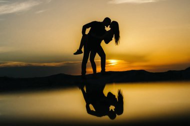 Gün batımında kucaklaşan sevgi dolu bir çiftin silueti.