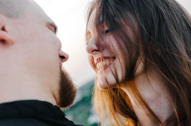 Yüzünde saçları olan güzel bir kız erkek arkadaşına bakıyor ve gülümsüyor.