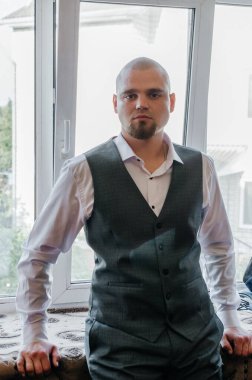 Beyaz gömlekli ve gri yelekli sakallı bir adamın portresi.