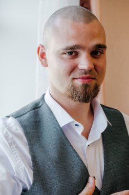 Beyaz gömlekli ve gri yelekli sakallı bir adamın portresi.