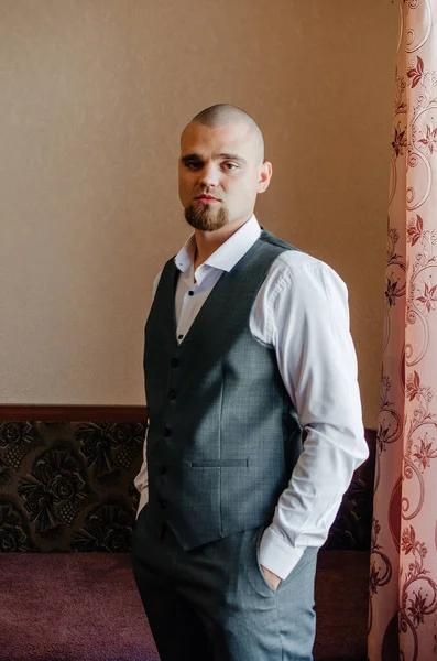 Beyaz gömlekli ve gri yelekli sakallı bir adamın portresi.