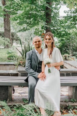 Gelin ve damat düğün buketi ile bankta oturuyorlar.