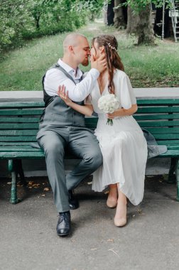  Gelin ve damat bir buketle bankta öpüşüyorlar.