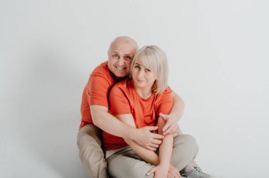 Turuncu tişörtlü çiftler beyaz arka planda gülüp sarılıyorlar.