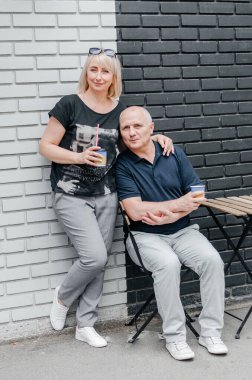 Bir adam ve bir kadın siyah ve beyaz bir duvarın yanında kahve içiyorlar.