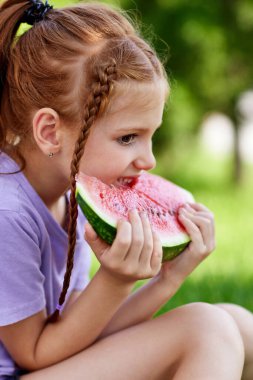Çocuk kız güneşli bir günde karpuz yiyor.