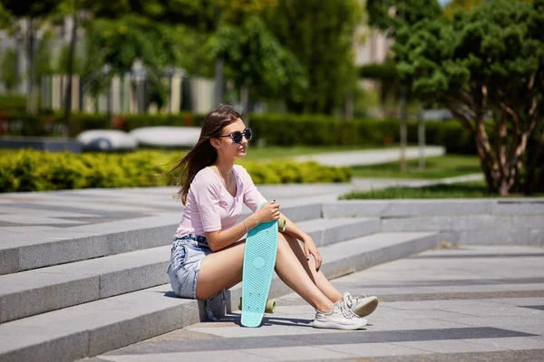Hermosa chica de skate con monopatín sentado al aire libre — Foto de Stock