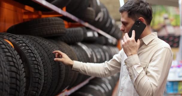 Cliente eligiendo neumáticos y consultando con alguien por teléfono — Vídeo de stock