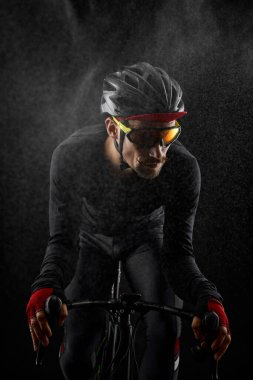 Erkek bisikletçi siyah arka planda bisiklet sürüyor.