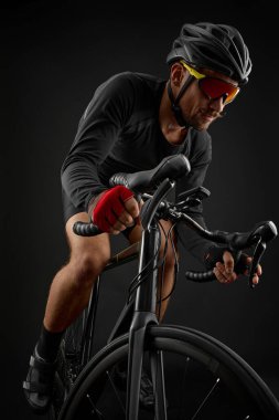 Erkek bisikletçi siyah arka planda bisiklet sürüyor.
