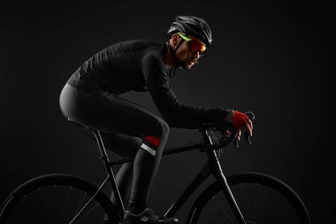 Erkek bisikletçi siyah arka planda bisiklet sürüyor.