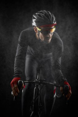 Erkek bisikletçi siyah arka planda bisiklet sürüyor.