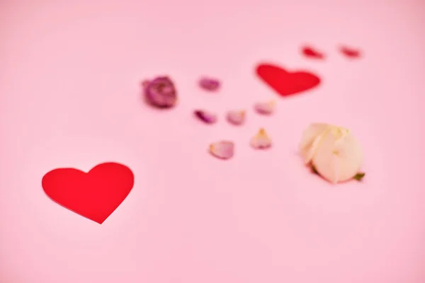 Rode papieren hartjes en rozenblaadjes op roze achtergrond. — Stockfoto