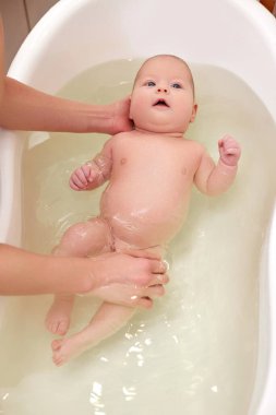 Anne bebeğini küçük plastik bir küvette yıkıyor.