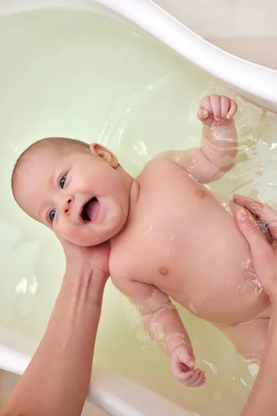 Madre baña a su bebé en una pequeña bañera de plástico blanco — Foto de Stock