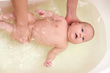 Anne bebeğini küçük plastik bir küvette yıkıyor.