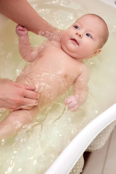 Moeder baadt haar baby in een wit klein plastic bad — Stockfoto