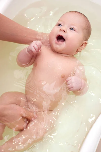 Madre baña a su bebé en una pequeña bañera de plástico blanco — Foto de Stock