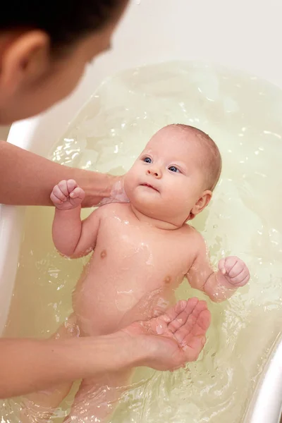Moeder baadt haar baby in een wit klein plastic bad — Stockfoto