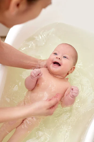 Mother bathes her baby in a white small plastic tub Royalty Free Stock Images