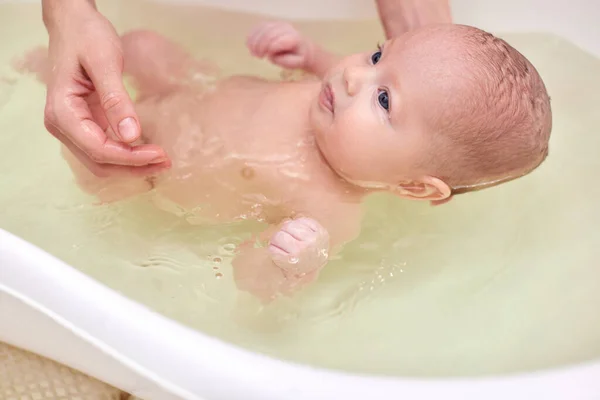 Mother bathes her baby in a white small plastic tub Royalty Free Stock Photos