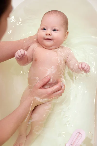 Matka koupe své dítě v bílé malé plastové vaně — Stock fotografie