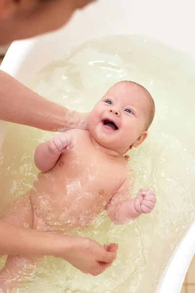 Mother bathes her baby in a white small plastic tub Stock Image