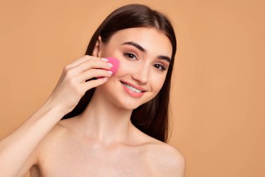Genç bir kadın pembe kozmetik süngerlerle poz veriyor.