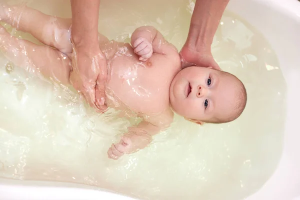 Mor badar sitt barn i en vit liten plastbadkar — Stockfoto