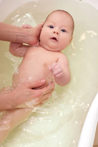 Mother bathes her baby in a white small plastic tub Stock Picture