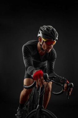 Erkek bisikletçi siyah arka planda bisiklet sürüyor.