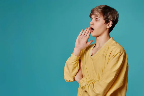 Ragazzo in maglione giallo tiene la mano vicino bocca chiamare qualcuno — Foto Stock