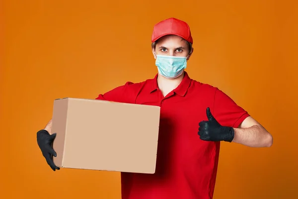 Dodavatel zaměstnanec v červené čepici obličejové masky, prázdná kartonová krabice — Stock fotografie