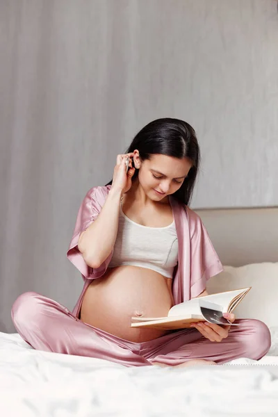 Mujer embarazada sentada en la cama y escribiendo en cuaderno — Foto de Stock