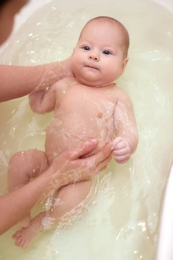 Anne bebeğini küçük plastik bir küvette yıkıyor.